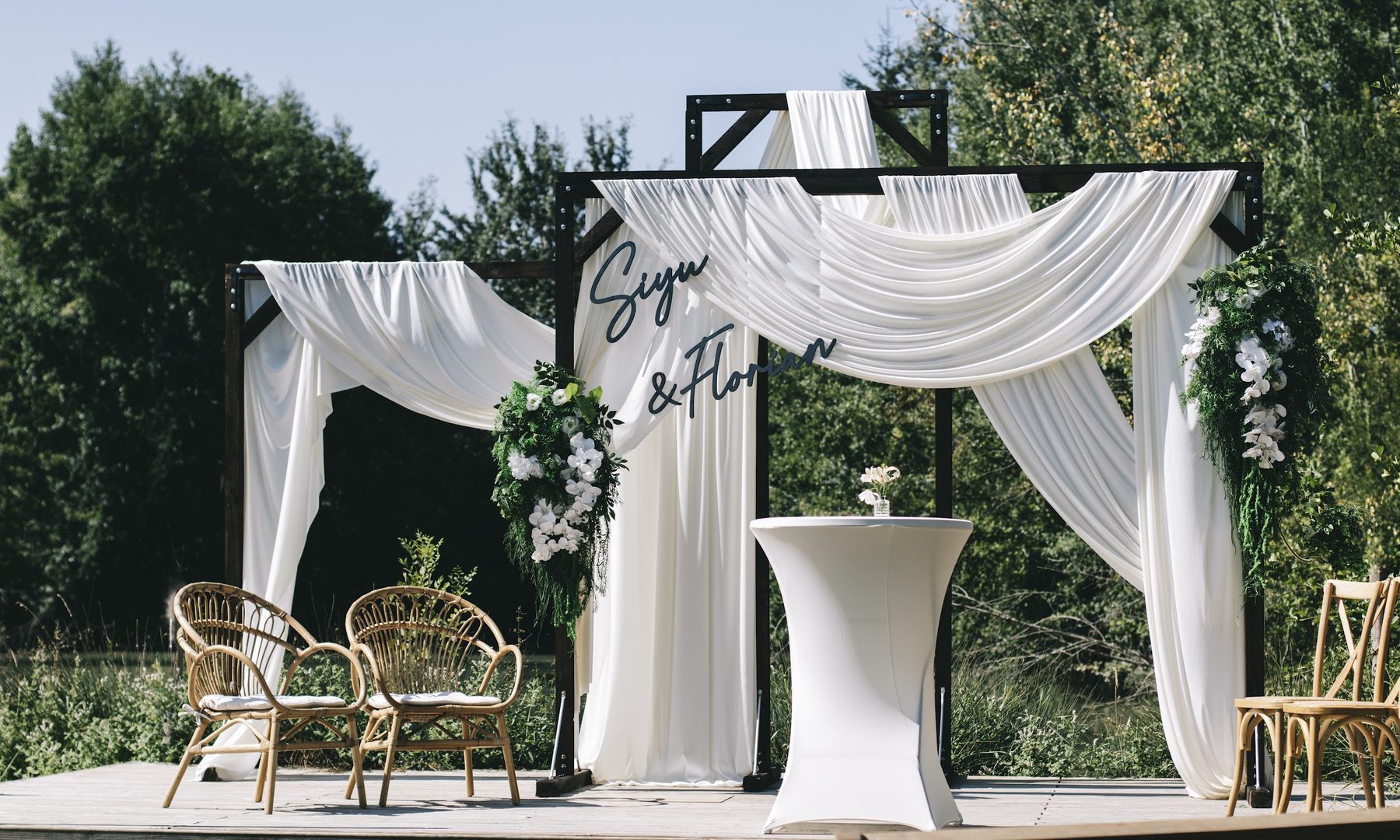 Structure en bois blanche drapée de tissu et de fleurs artificielles, construite par Potier & Fils pour un mariage
